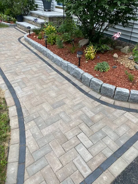 Herringbone paver walkway with granite border and fresh plantings by Miller Mowing & Landscape