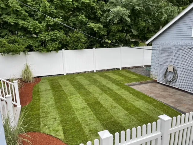 Freshly striped lawn behind a white picket fence, mowed by Miller Mowing & Landscape